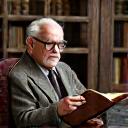 An older, distinguished historian holding a book, engaging with a traveler in a library setting.